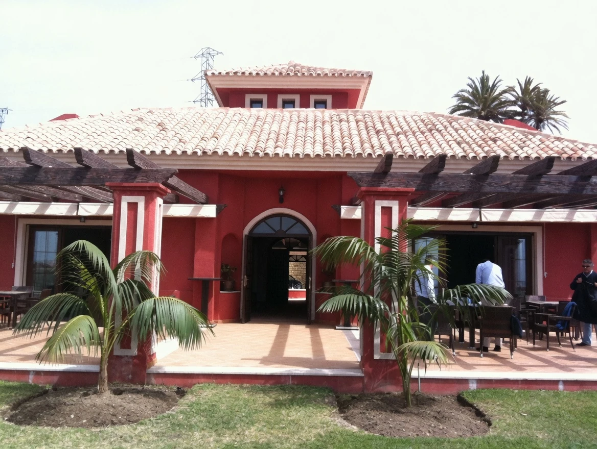 Villa de fachada roja con pérgola de madera y palmeras, Costa del Sol